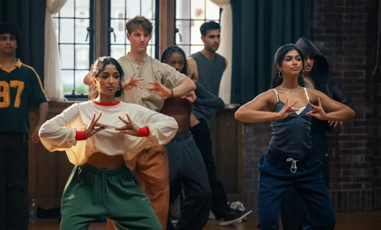 "A diverse group of young adults practicing dance in a studio with wooden floors, brick walls, and large windows. The two women in the front are focused on their hand movements, suggesting a choreographed routine."
